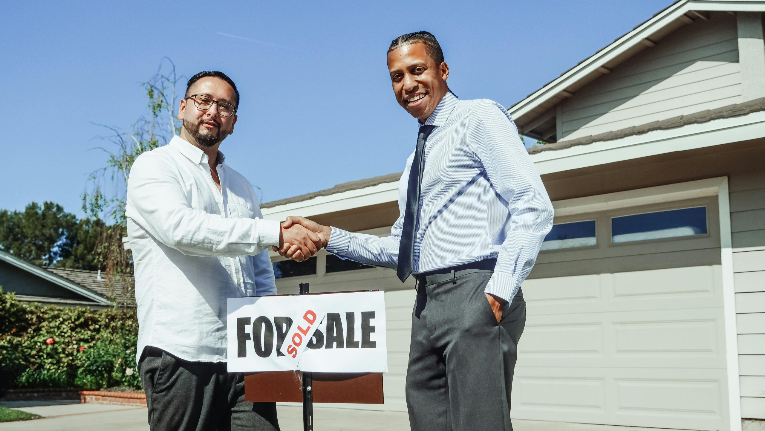 real estate agent shaking hands with a client in front of a yard sign with "SOLD" on it