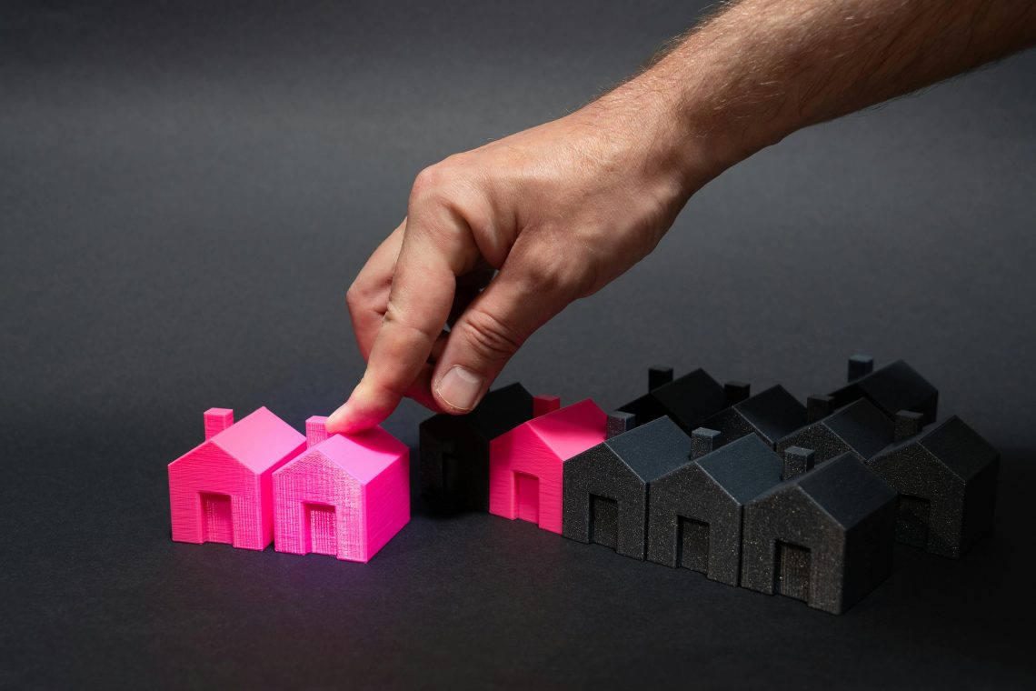 hand pointing at a pink house model surrounded by other pink and black house models
