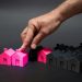 hand pointing at a pink house model surrounded by other pink and black house models