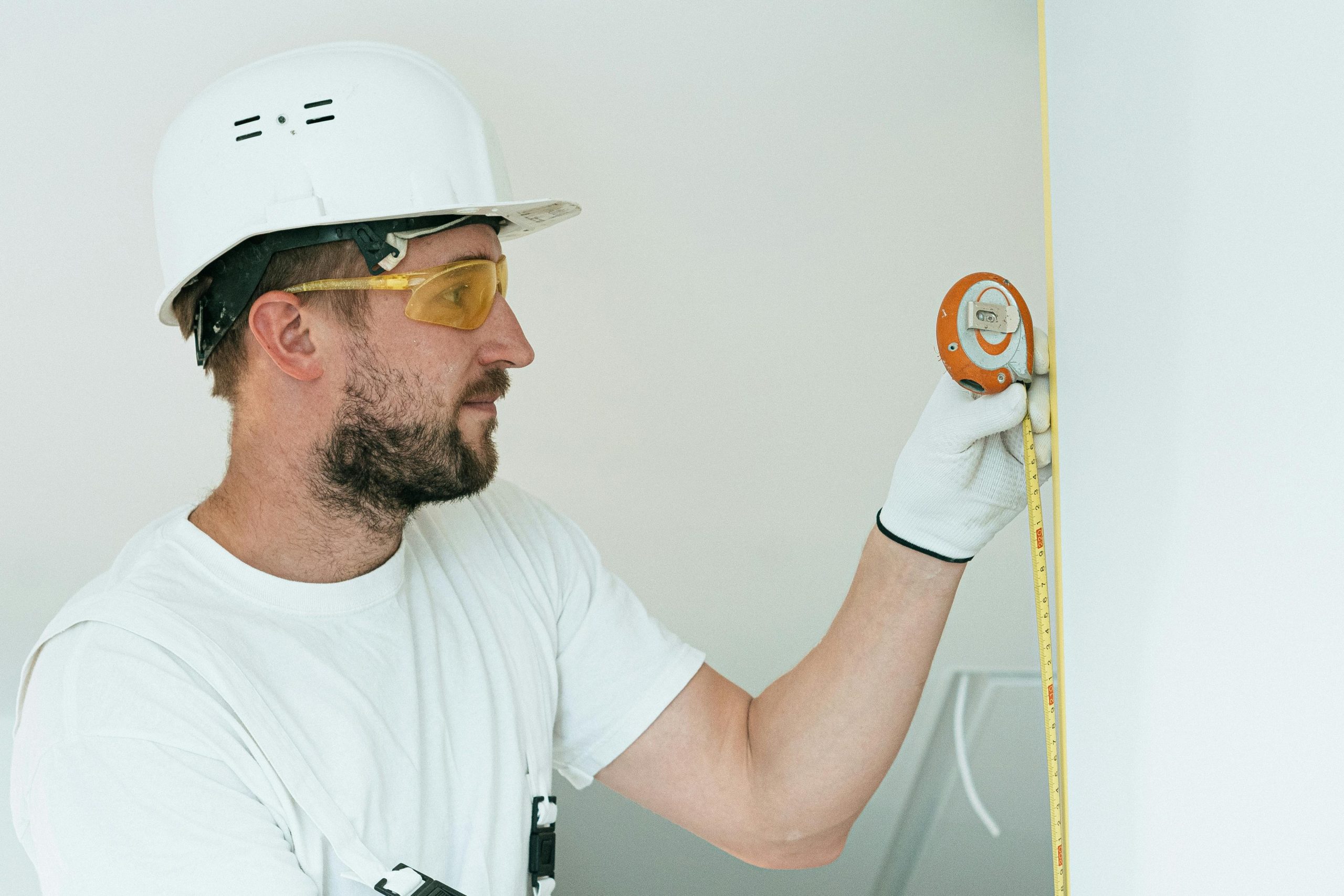 man in a white hard hat measuring a wall